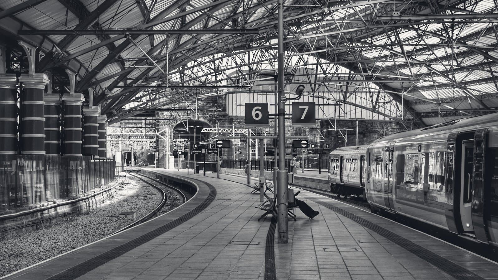 A Victorian railway station under an iron and glass roof, a train standing at platform 7 on the right while the curved track at platform 6 on the left lies empty.