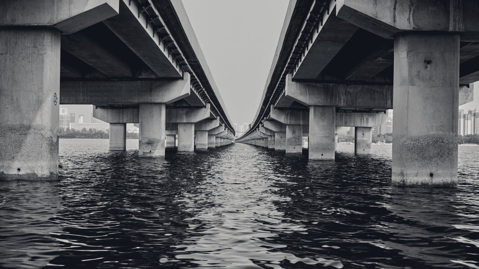 Two long concrete viaducts running side by side over open water, seen from the surface between them, their rows of piers converging toward the horizon.
