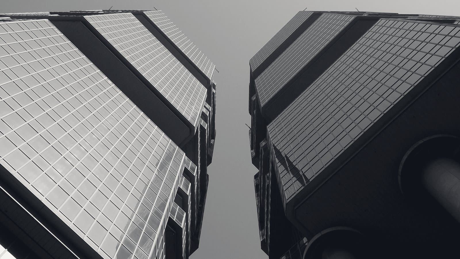 Two glass office towers seen from below, facing each other across a narrow gap of sky, their mirrored facades catching the light.